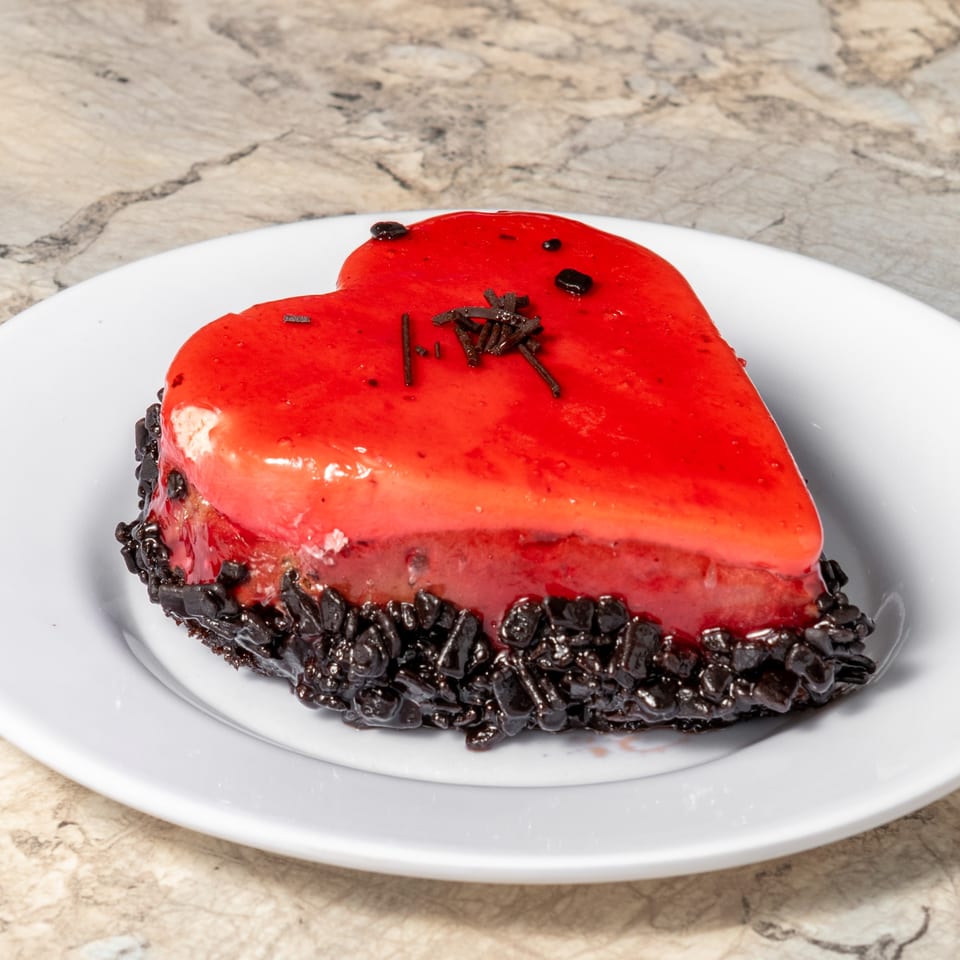 Heart-shaped cake with red glaze and chocolate sprinkles on a white plate.